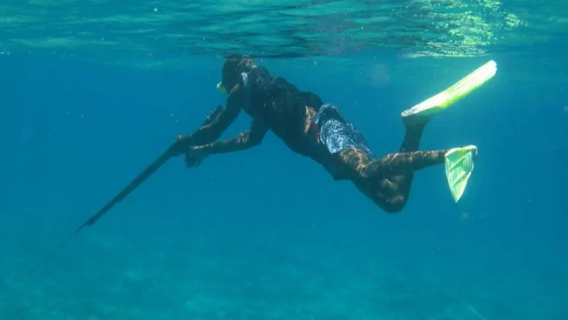 A Papua New Guinean spear fisherman loading a rifle-style spear gun at the surface. These spear guns are normally hand carved wooden stocks with rubber slings that fire a thin metal rod that has been hand sharpened.