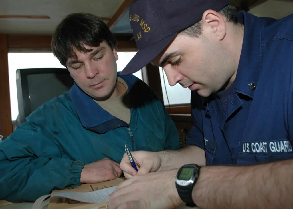 Coast Guard Petty Officer 3rd Class Dan Jarrett, of Marine Safety Detachment Kodiak, goes over the results of the dockside safety exam with the captain of the fishing vessel Castle Cape, Steve Eggemeyer in 2006. Credit: Petty Officer Paul Roszkowski