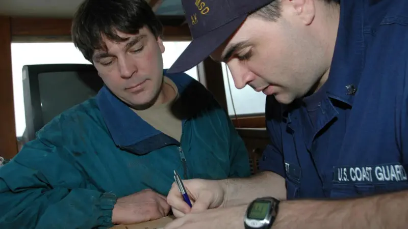 Coast Guard Petty Officer 3rd Class Dan Jarrett, of Marine Safety Detachment Kodiak, goes over the results of the dockside safety exam with the captain of the fishing vessel Castle Cape, Steve Eggemeyer in 2006. Credit: Petty Officer Paul Roszkowski