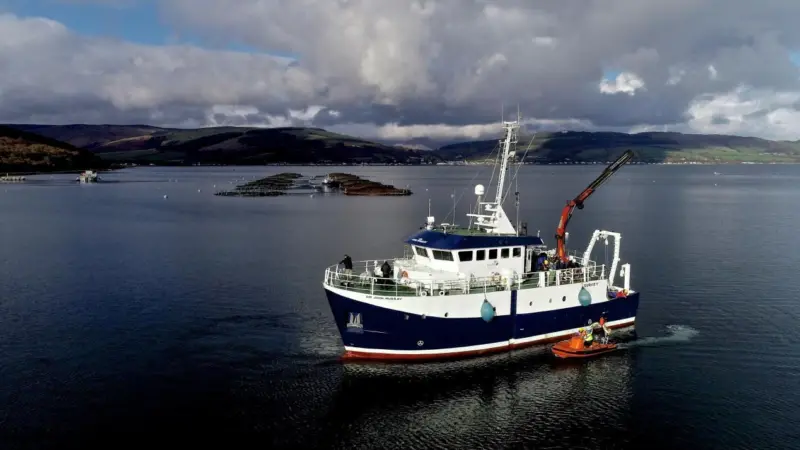 A survey vessel on the west coast of Scotland with a salmon farm in the background
