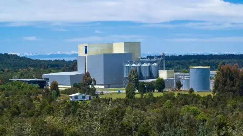 Image of BioMar's feed production factory in Ercilla, Chile with trees in the foreground, mountains in the back on a sunny day