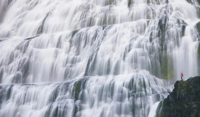 Very small person in red looking at a large waterfall