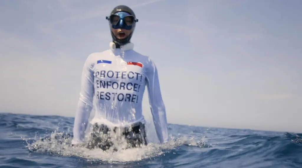 Alessia Zecchini, freediver, wearing a vest saying PROTECT! ENFORCE! RESTORE! to protest against French bottom trawling