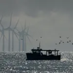 Image of a fishing boat with offshore wind turbines in the background