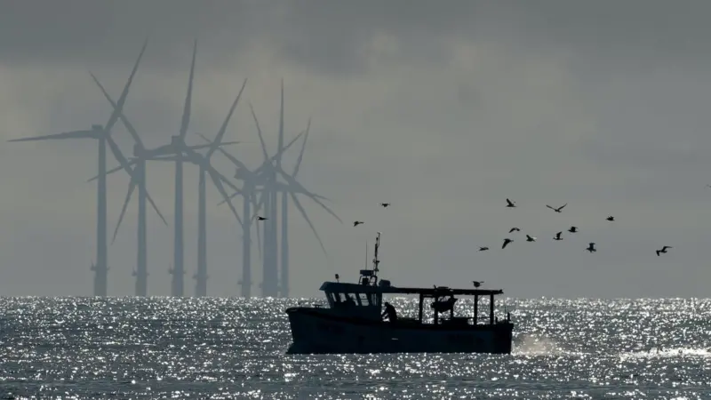 Image of a fishing boat with offshore wind turbines in the background