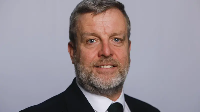 The image shows a headshot of Finlay Carson MSP in a black suit and tie