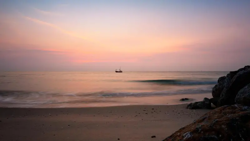The picture shows a traditional fishing boat on water at sunrise