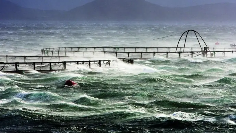 Fish pens in a stormy sea with mountains behind