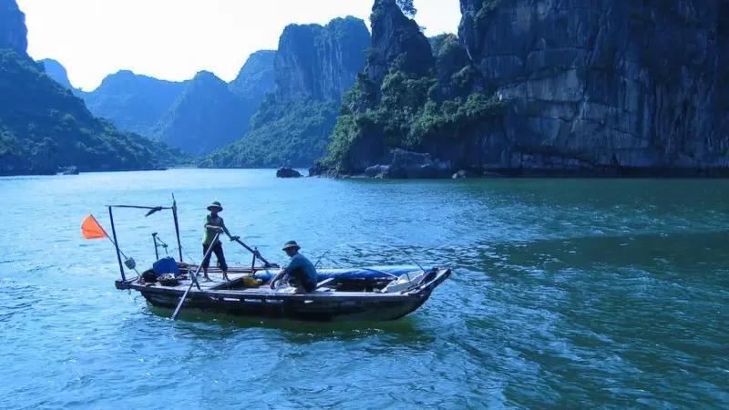 Vietnamese fishing boat with two fishers and cliffs in the background