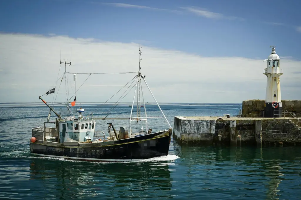 Small fishing vessel next to a harbour wall with tiny lighthouse