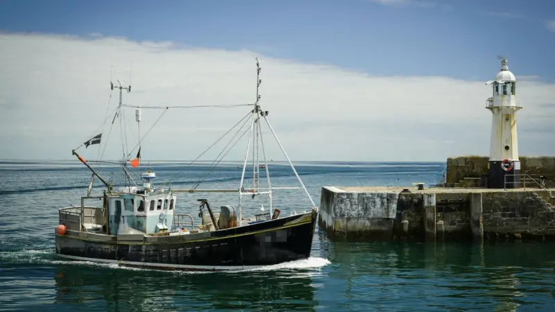 Small fishing vessel next to a harbour wall with tiny lighthouse