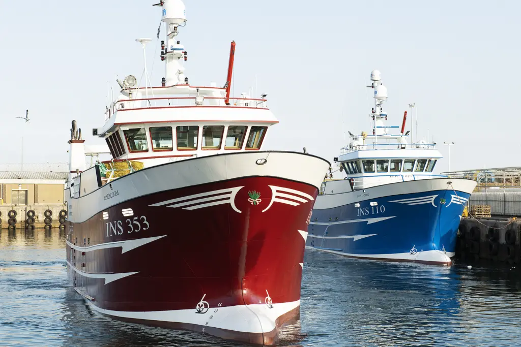 Two fishing vessels dockside, one with a blue hull and one with a red hull