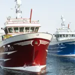 Two fishing vessels dockside, one with a blue hull and one with a red hull