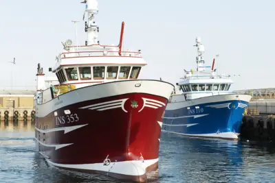Two fishing vessels dockside, one with a blue hull and one with a red hull